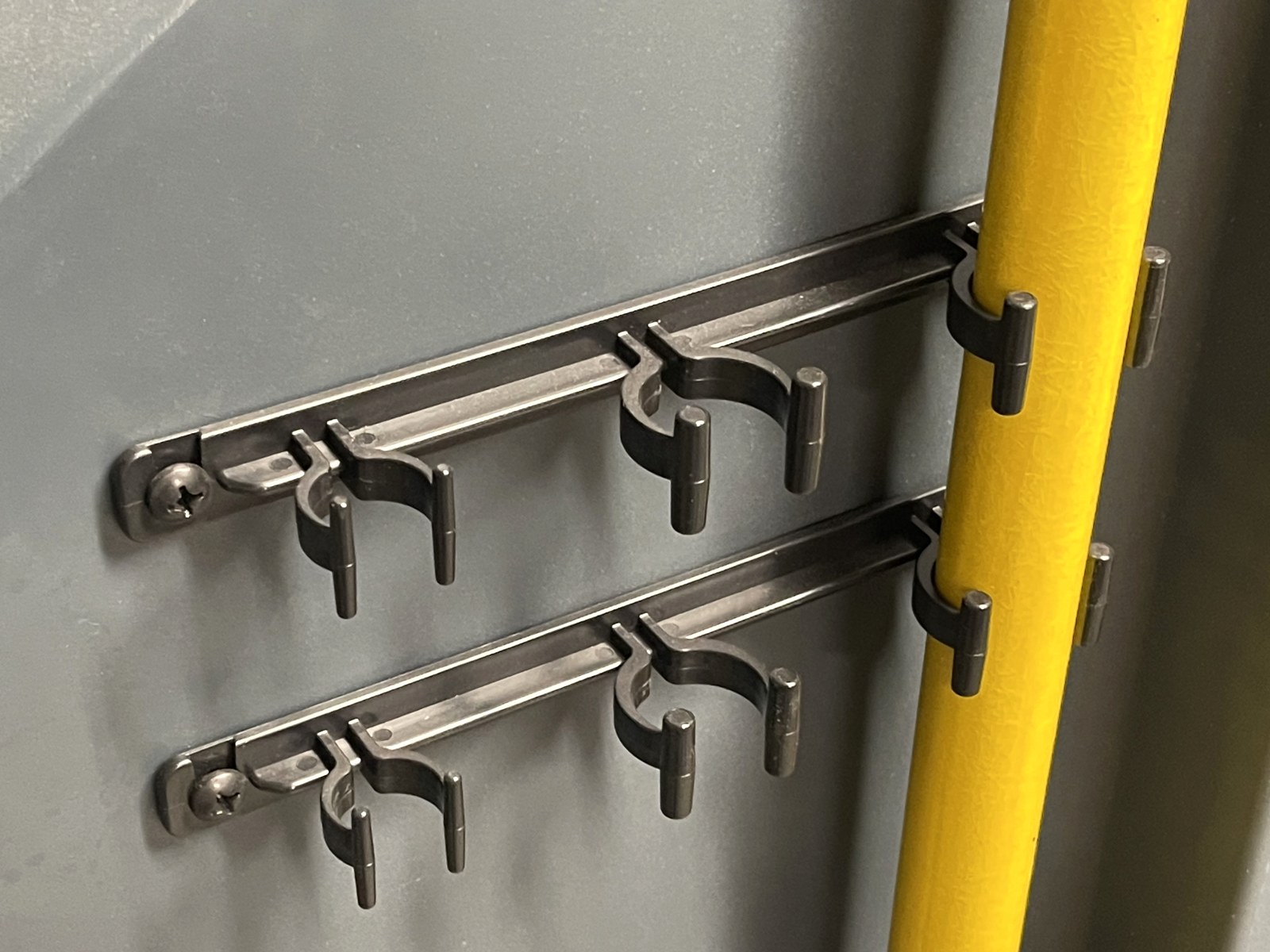 Two molded clip brackets on a janitorial cleaning cart holding a yellow handle